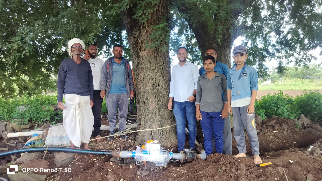 Community demonstration of water conditioner installation under large tree with multiple farmers